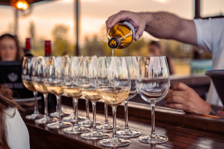 Barman pouring white wine at a wooden counter at sunset, Pamplona pintxo bar style