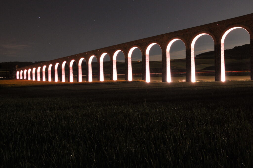 Illuminated arches of the Acueducto de Noáin lit up at night near Pamplona