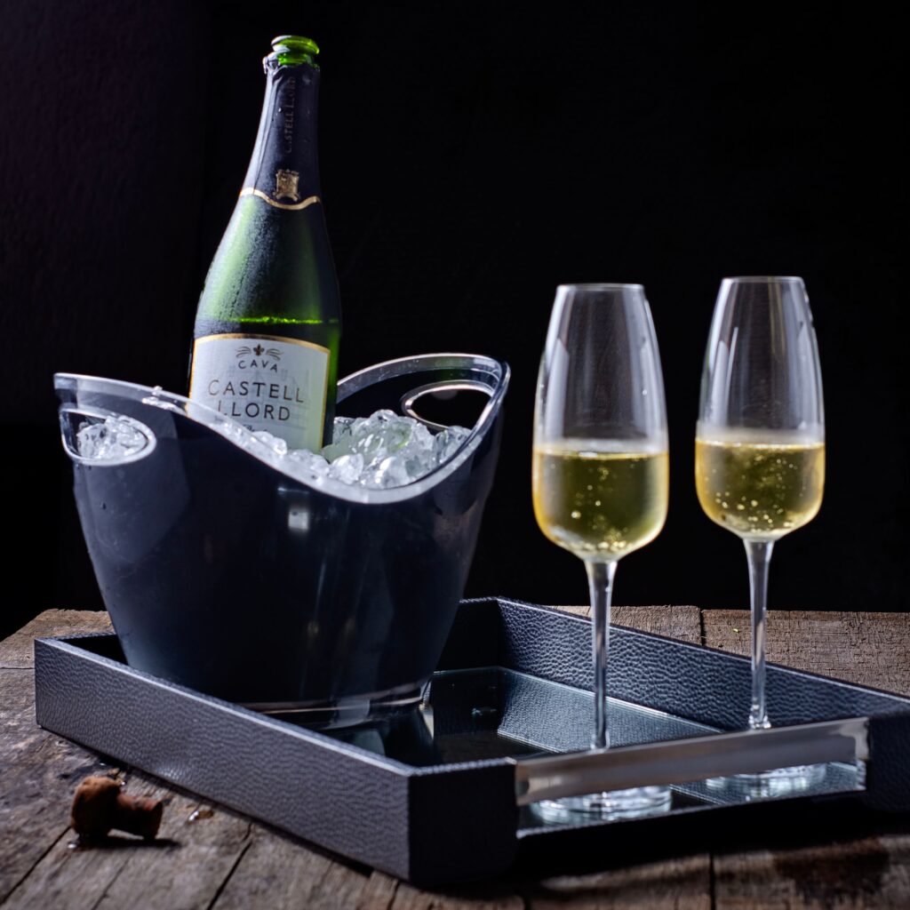 Chilled bottle of cava with two filled flutes on a black tray
