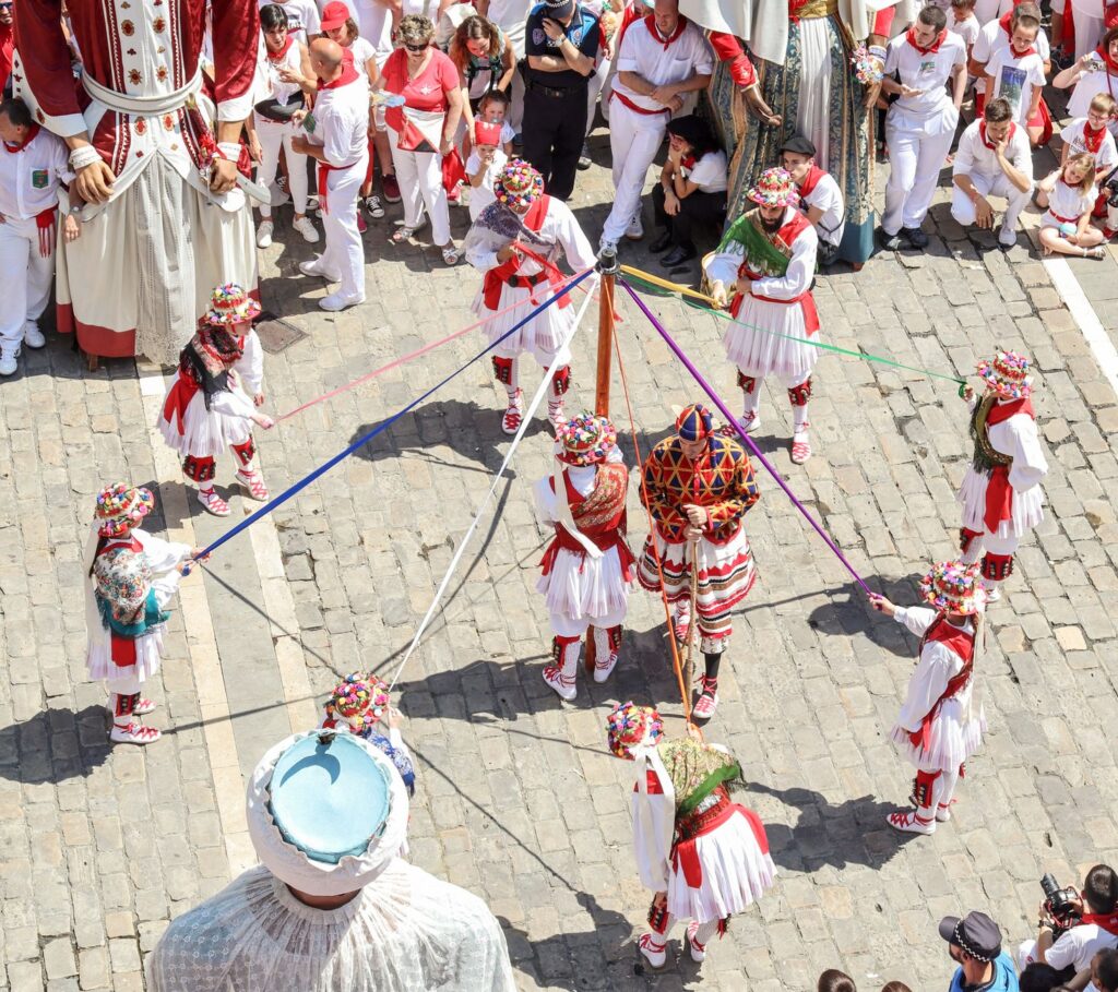 Traditional Navarrese folk dancers in red and white costume perform a maypole ribbon dance in Pamplona