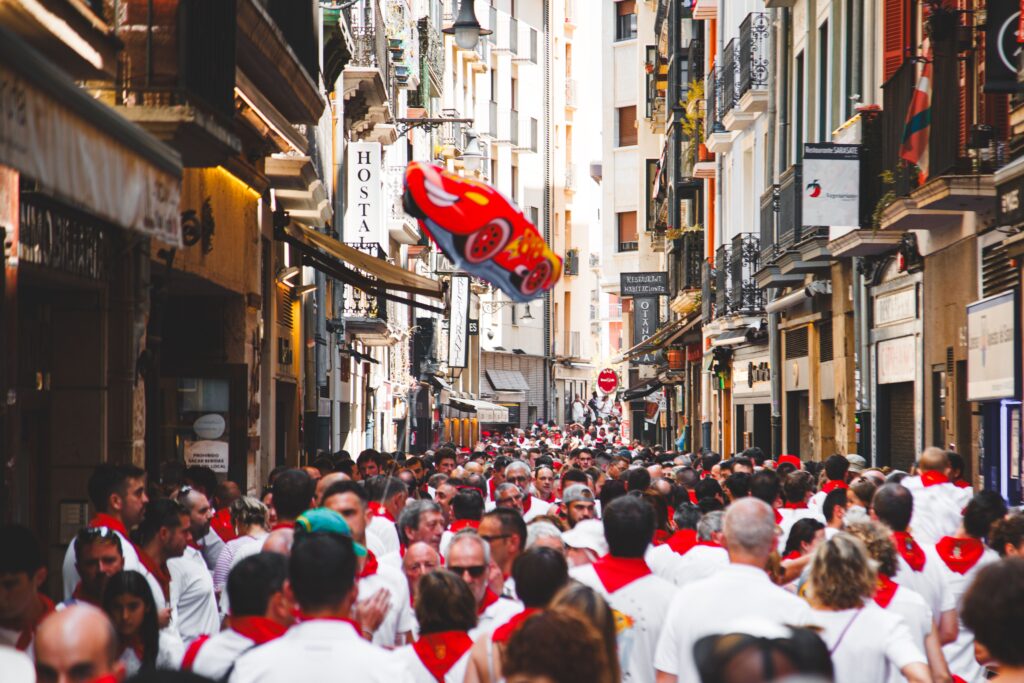 Crowd of San Fermin festivalgoers in white and red filling a lodging-lined Pamplona street