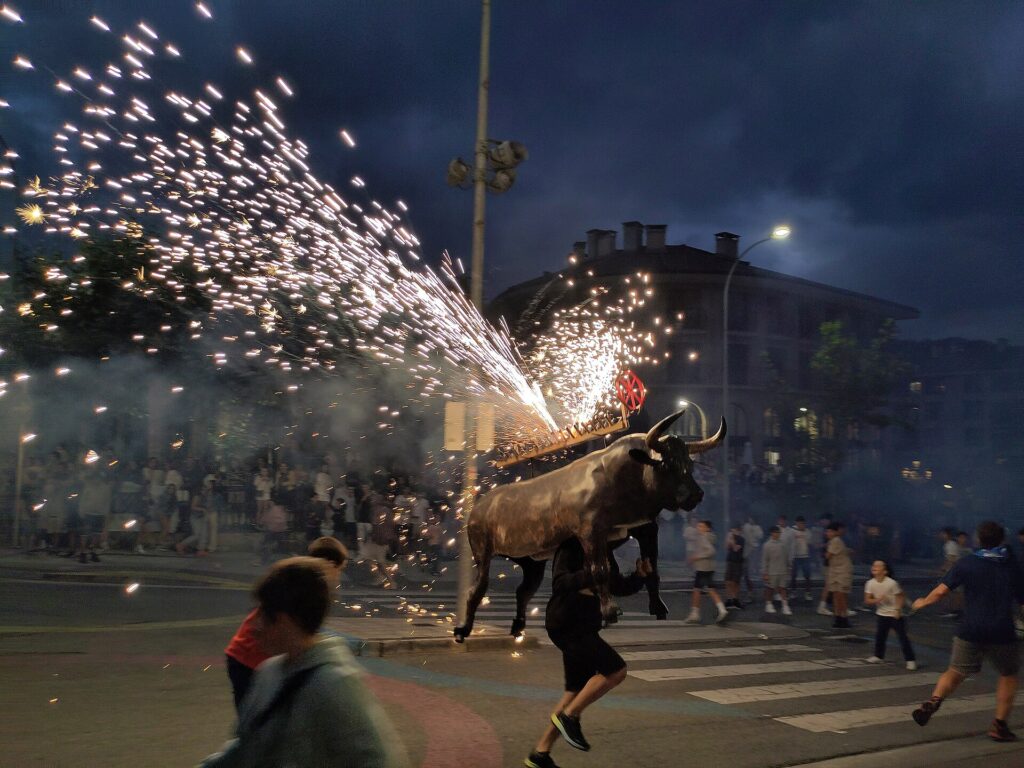 Toro de fuego bull frame showering sparks as children run ahead at a Basque fiesta at dusk